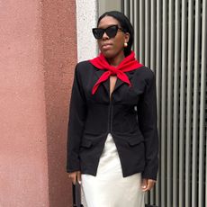 Woman wears black blazer, cream skirt and red knitted triangle scarf