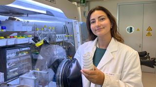 ETH doctoral student Marie Perrin presents the new recycling approach. In her left hand, she is holding the raw material in the form of a fluorescent lamp and, in her right, the yellow reagent that can separate rare earth metals. 