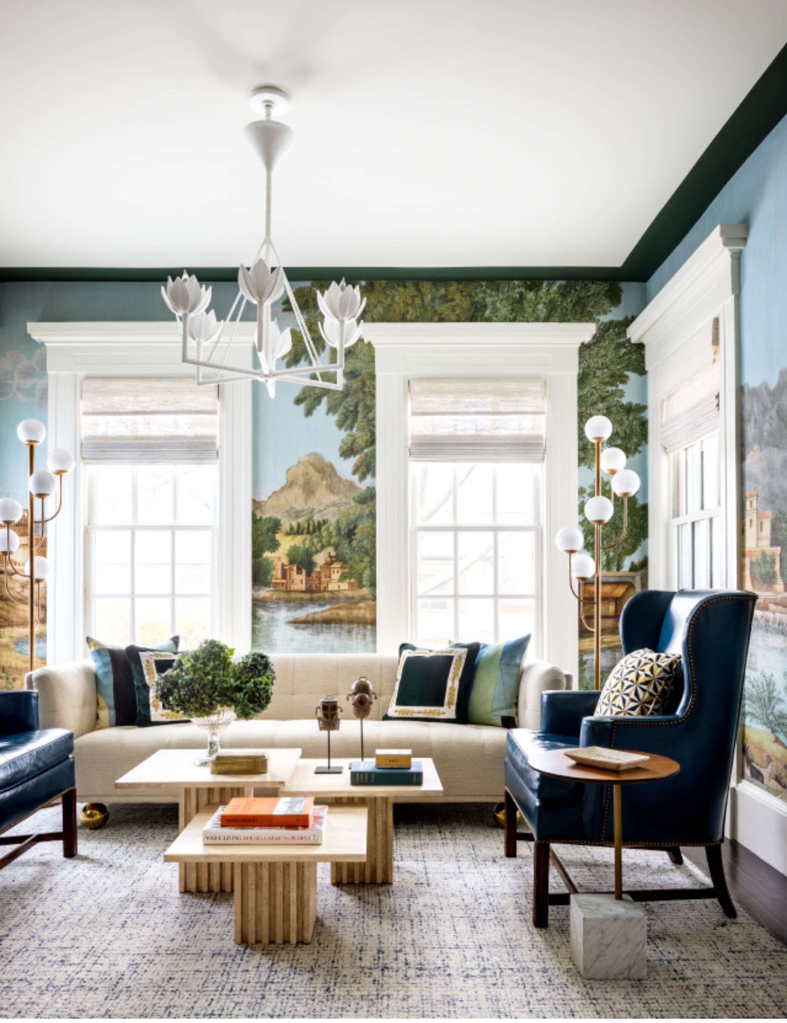 Storied living room featuring nature-inspired wallpaper, a modern floral chandelier, and seating in navy and cream