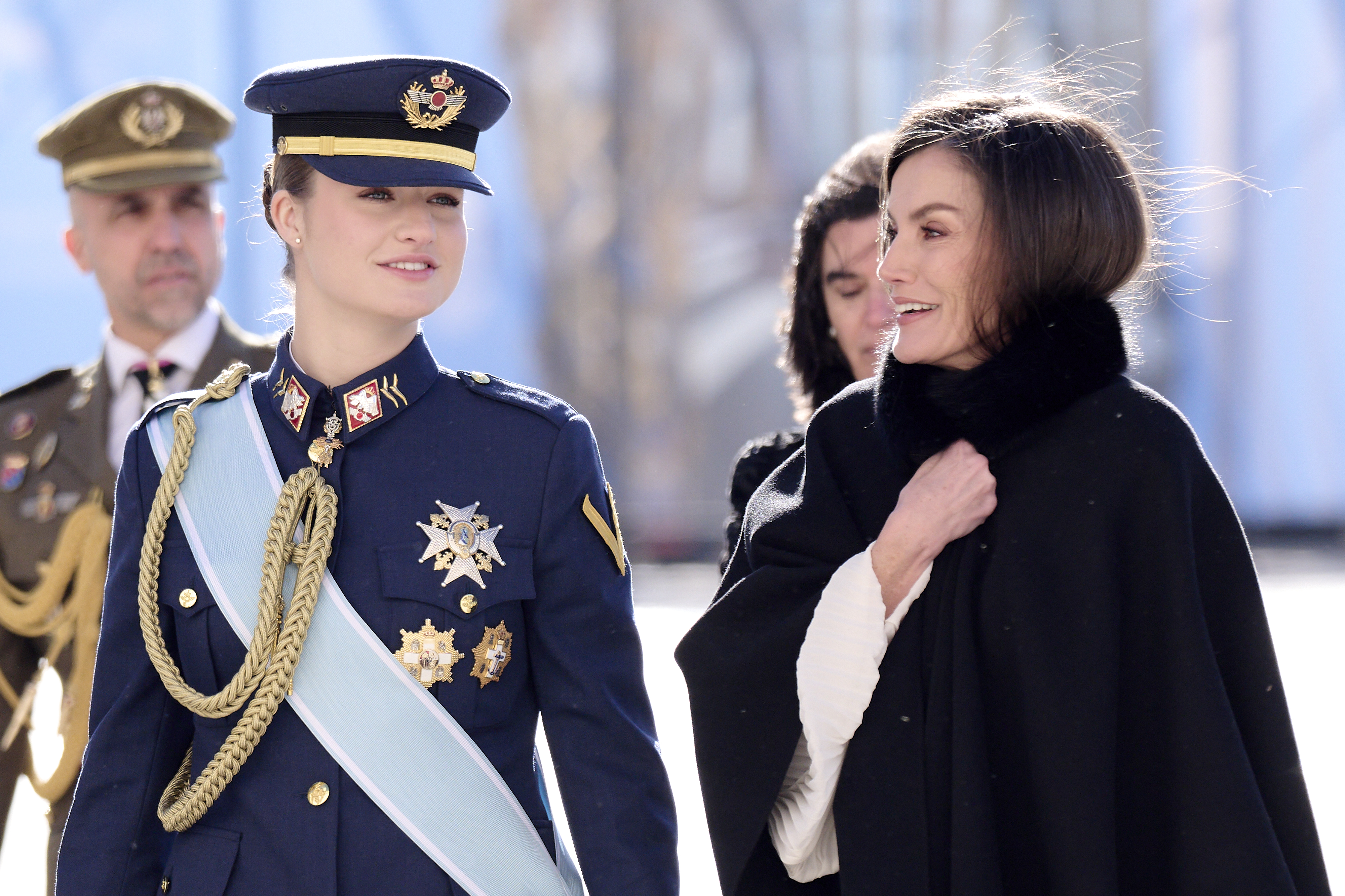 Princess Leonor in a military uniform next to Queen Letizia, clutching the neck of a black fur coat