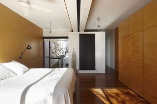 Alternative view of a bedroom at Moor Street House featuring white and wood panelled walls, wood flooring, a bed with white pillows and linen, a window, a wall lamp, a white ceiling fan, pendant lights, a tall black radiator and a decorative model of a building on the lower part of the wall