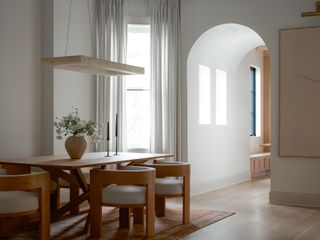 A spare dining room with rounded dining chairs and an arched hallway in the background