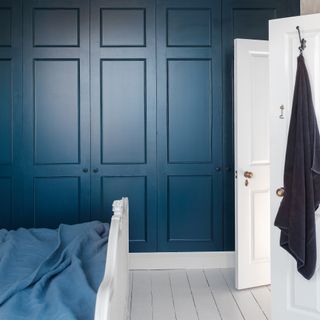 A bedroom with a white floor and paintwork and a panelled navy feature wall