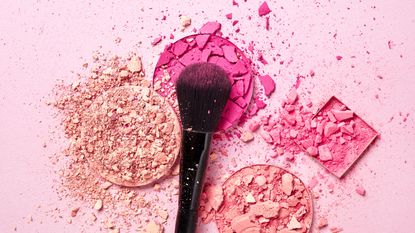 Crushed face powders and makeup brush on pink background