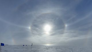 Rings of sunlight reflect against a snowy surface with a bright cloudy sky
