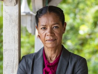 Jaye Griffiths in character as DI Karen Flitcroft, standing on the beach with the trees behind her