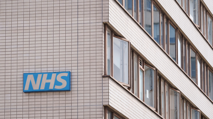 A gray tiled building with rows of windows and the blue NHS logo on the side