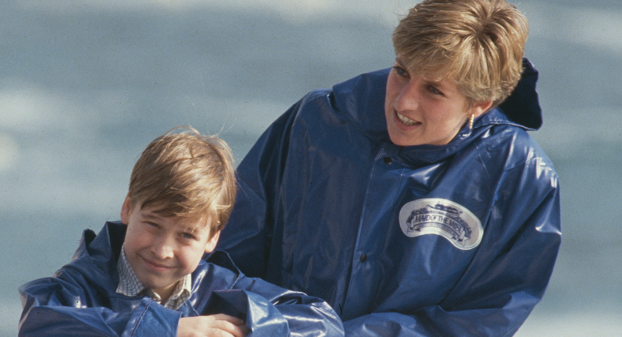 Prince William and Princess Diana both wear blue rain coats and have similar dusty blond hair