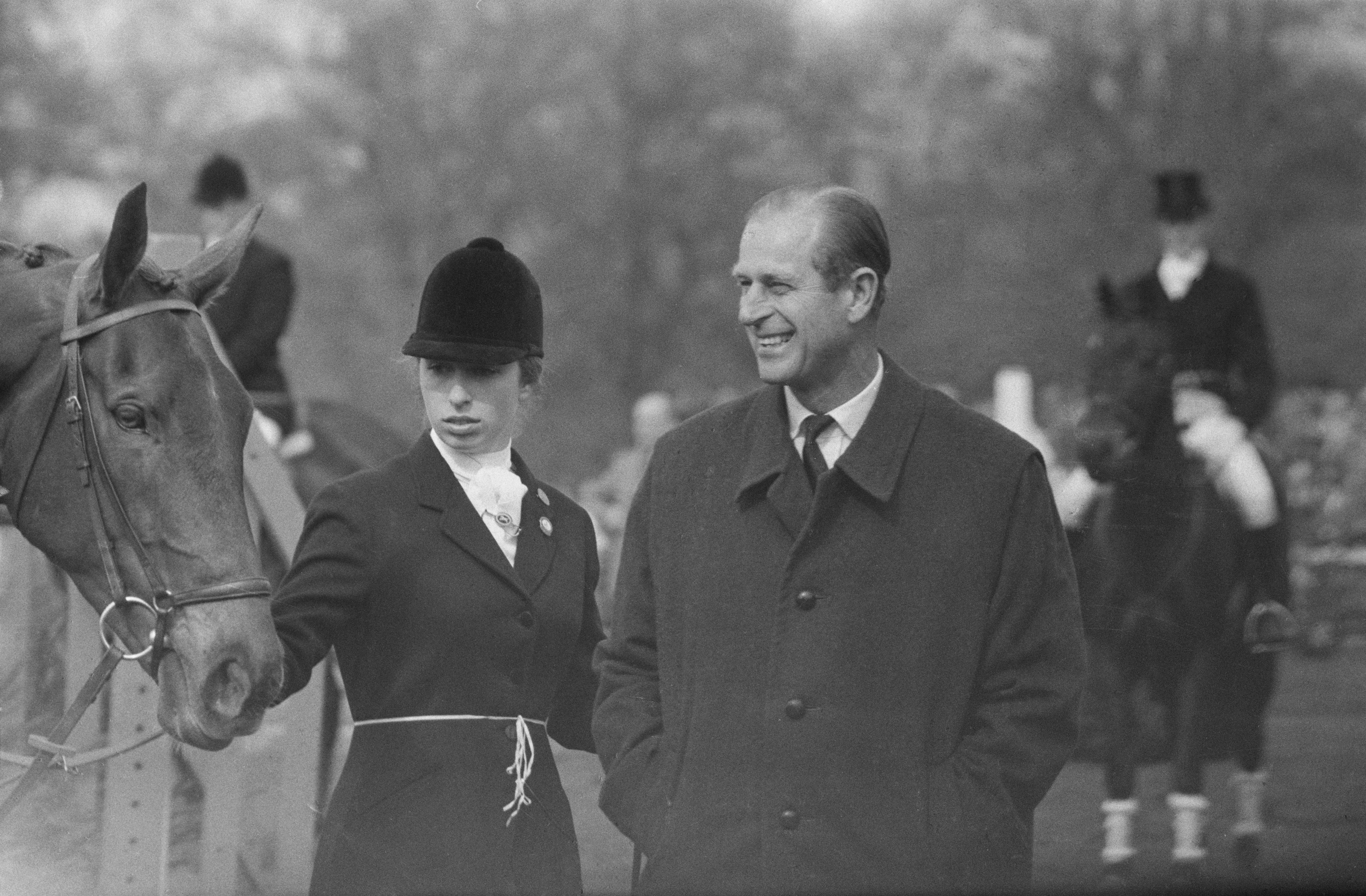 Princess Anne wearing an equestrian outfit standing with her horse and Prince Philip, who is laughing