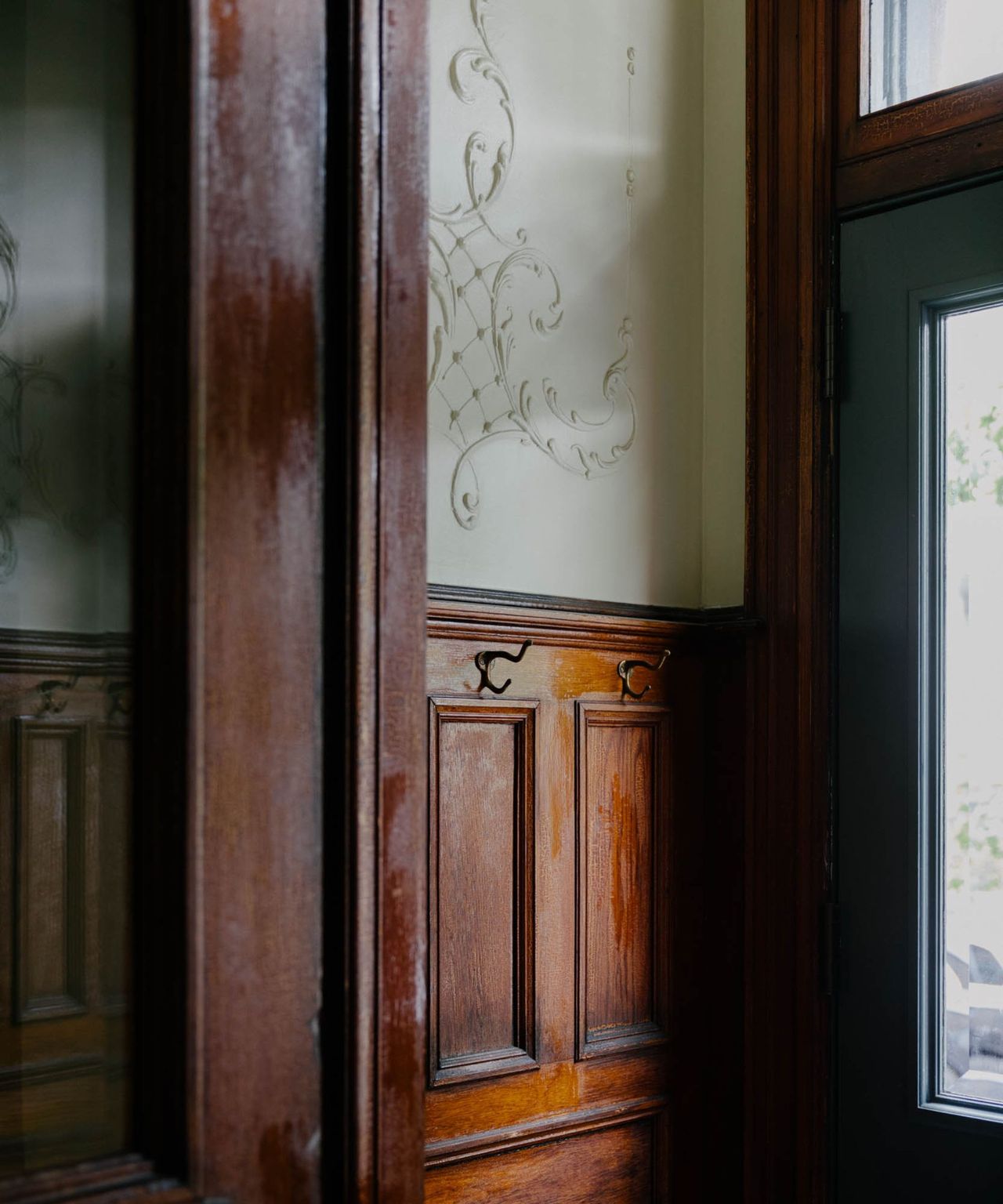 An antique door made of dark wood and glass with two hooks