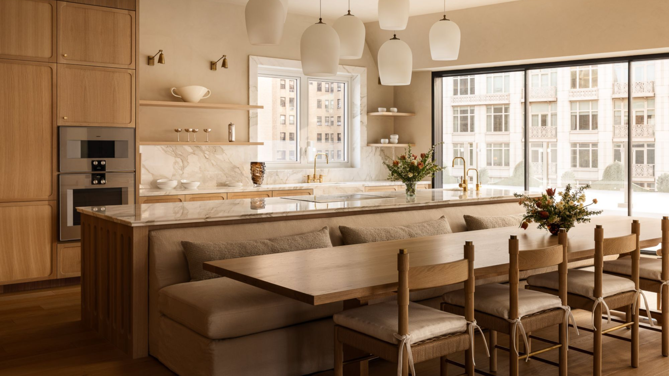 A modern timber kitchen with fluted detailing on the cabinetry, a marble worktop and island with several pendant lights hanging above and with built-in seating on the dining table side