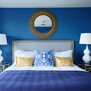 Blue bedroom with a round mirror above the bed and two white lamps on the bedside table
