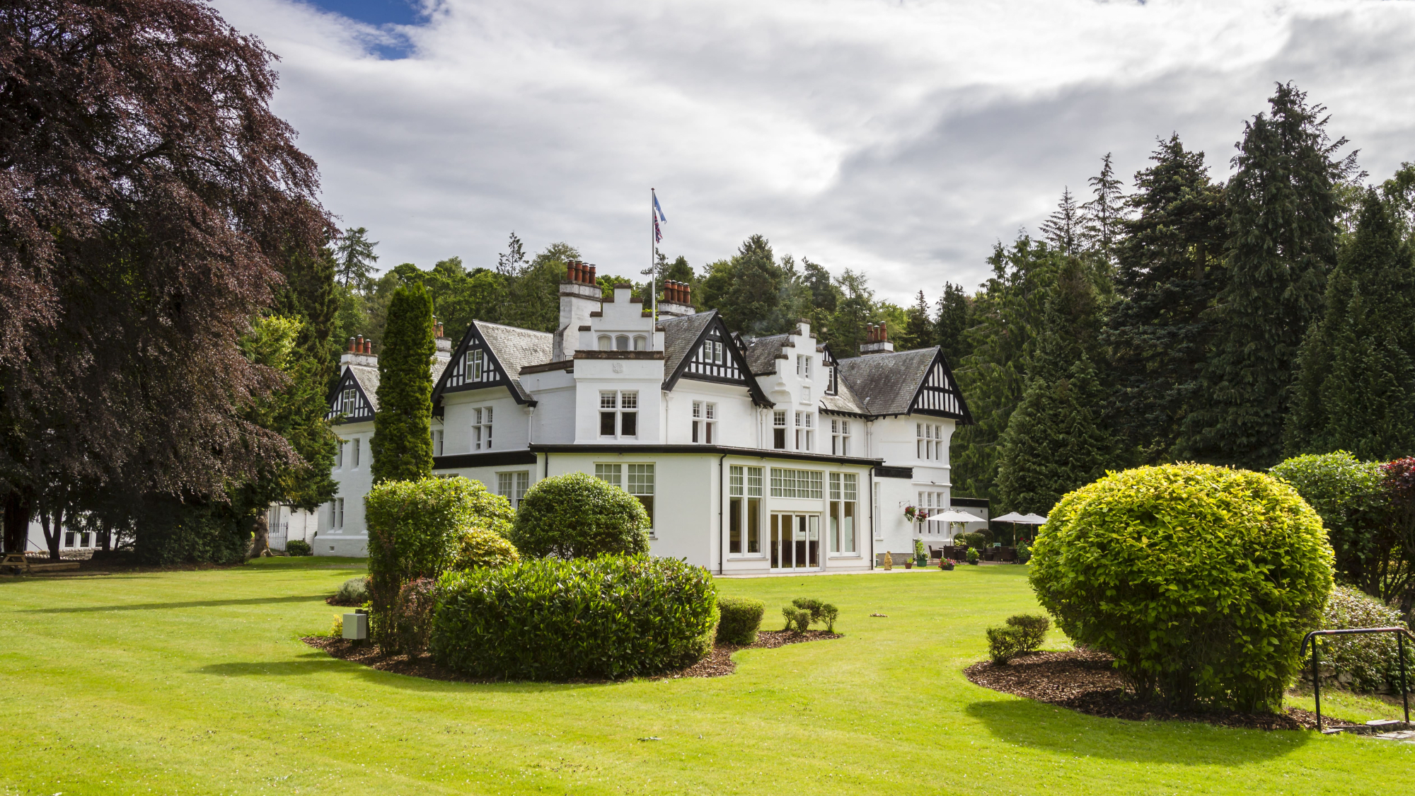 White-painted exterior of Pine Trees Hotel, Pitlochry, surrounded by lawns and mature trees