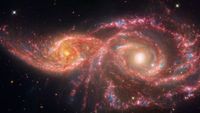 two swirling galaxies in deep space glow in shades of red and yellow