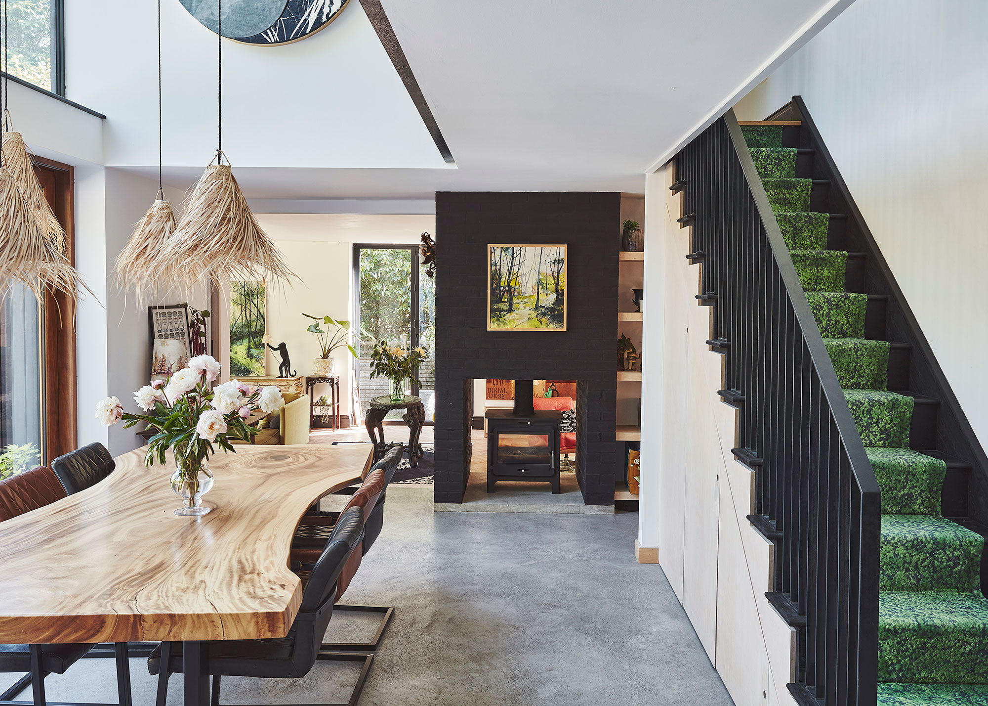 open plan dining room with poured concrete floor and wicker pendant lights with green carpeted staircase