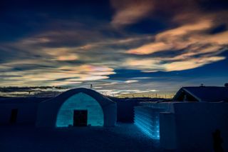Nacreous clouds shine at twilight above the ice hotel below.
