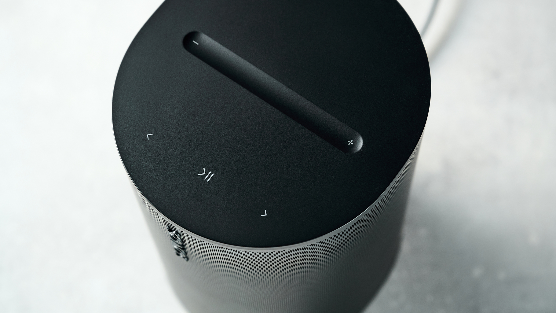A closeup of the Sonos Era 100 SL from above, showing the play/pause and skip buttons and volume bar on top.