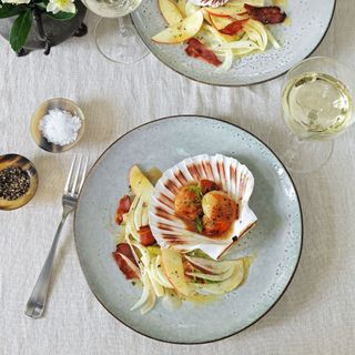 Scallops with brown butter dressing on light blue plates and white linen tablecloth