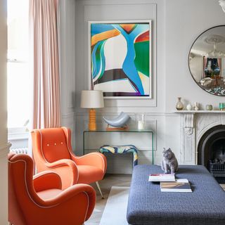 Living room with red upholstered armchairs in bay window, grey walls with cornice and marbled mantelpiece, modern art and circular mirror