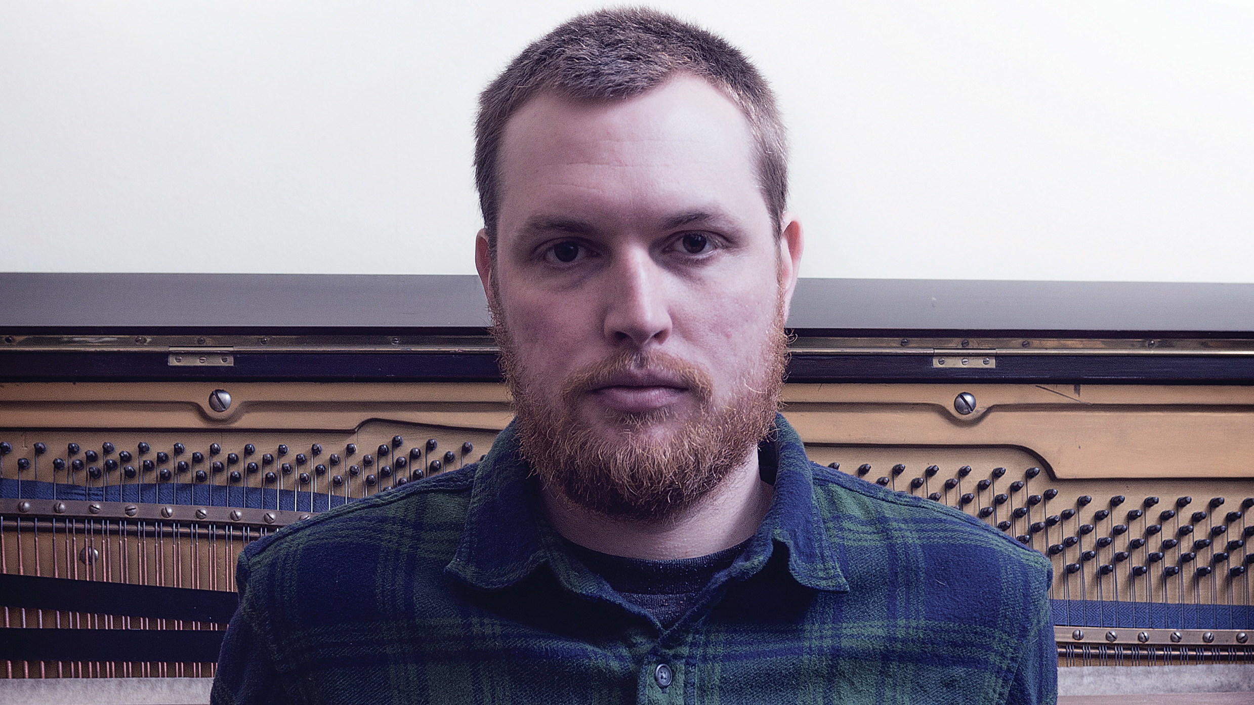 Ben Chatwin poses next to the inside of a piano