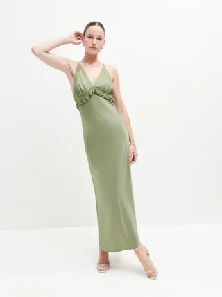 a model wears a sage green satin dress in front of a plain backdrop