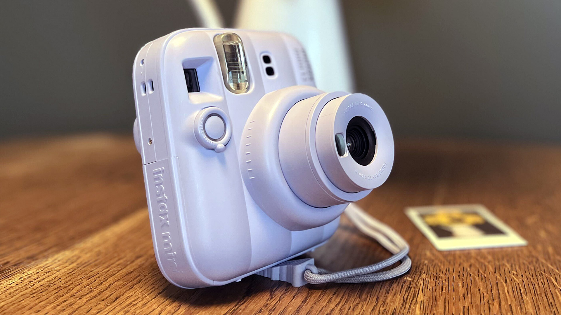 The Frost Blue Instax Mini 13 on a table next to a vase with a print laid beside it