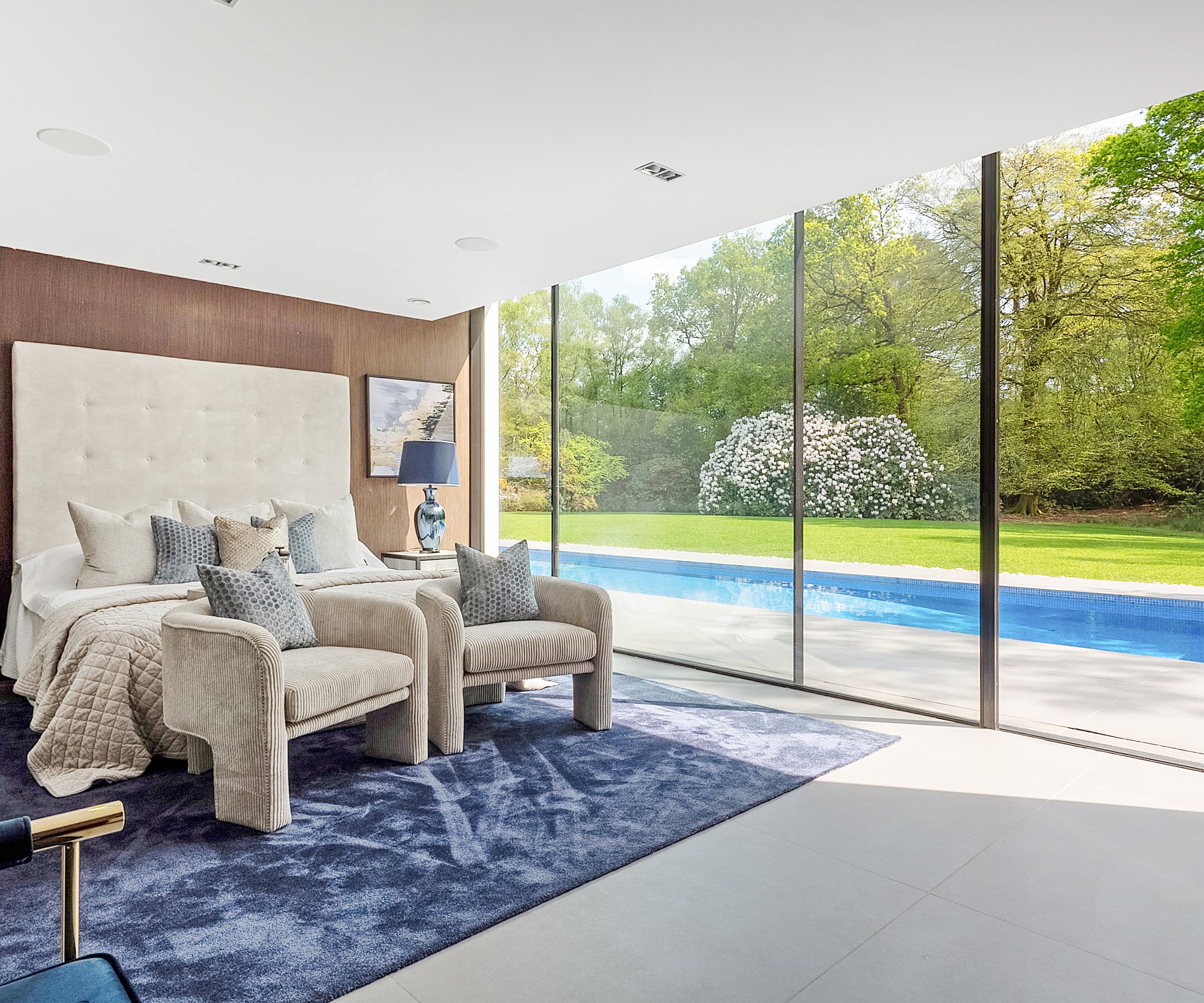 A master bedroom with grey sheets with bifold doors leading to a swimming pool