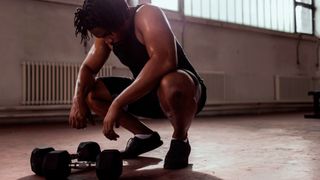 Man crouches over a pair of dumbbells