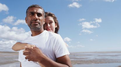 A couple on the beach look pensively at the horizon.