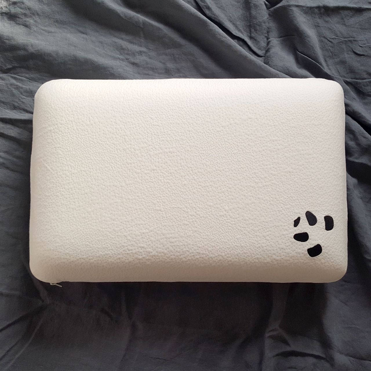 The Panda Memory Foam pillow lying flat with the logo showing on grey bed linen