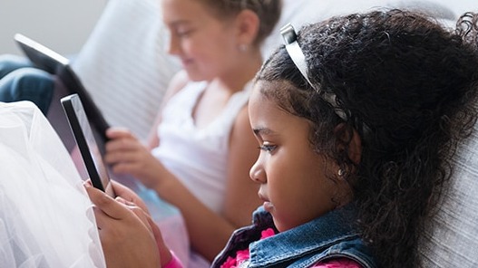 Two young girls, one on a phone and the other on a tablet.