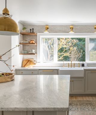 white and gray kitchen with open shelving on one side, brass hardware and lighting, rug, tiled wall