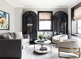 Living room with white walls, grey and neutral seating, and two black curved cabinets either side of a window