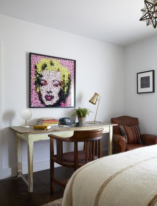 guest room office with rustic desk and mahogany chair, leather armchair in corner, bed in foreground, Marilyn Monroe print, brass desk light