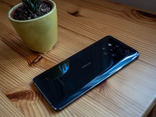 The Nokia 9 Pureview on a wooden table with a cup of iced tea sat next to it