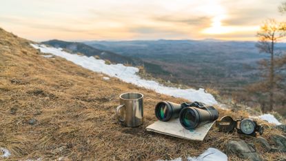 Binoculars map compass and mug on the background of nature mountains in the sunset. 