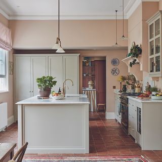 Cream kitchen with island, terracotta floor tiles and pendant lights