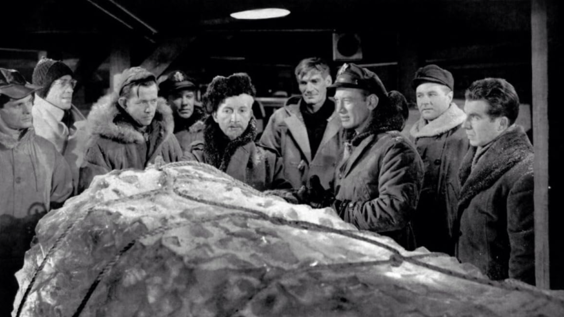 A group of men are crowded around a giant ice block thats under rope restraints