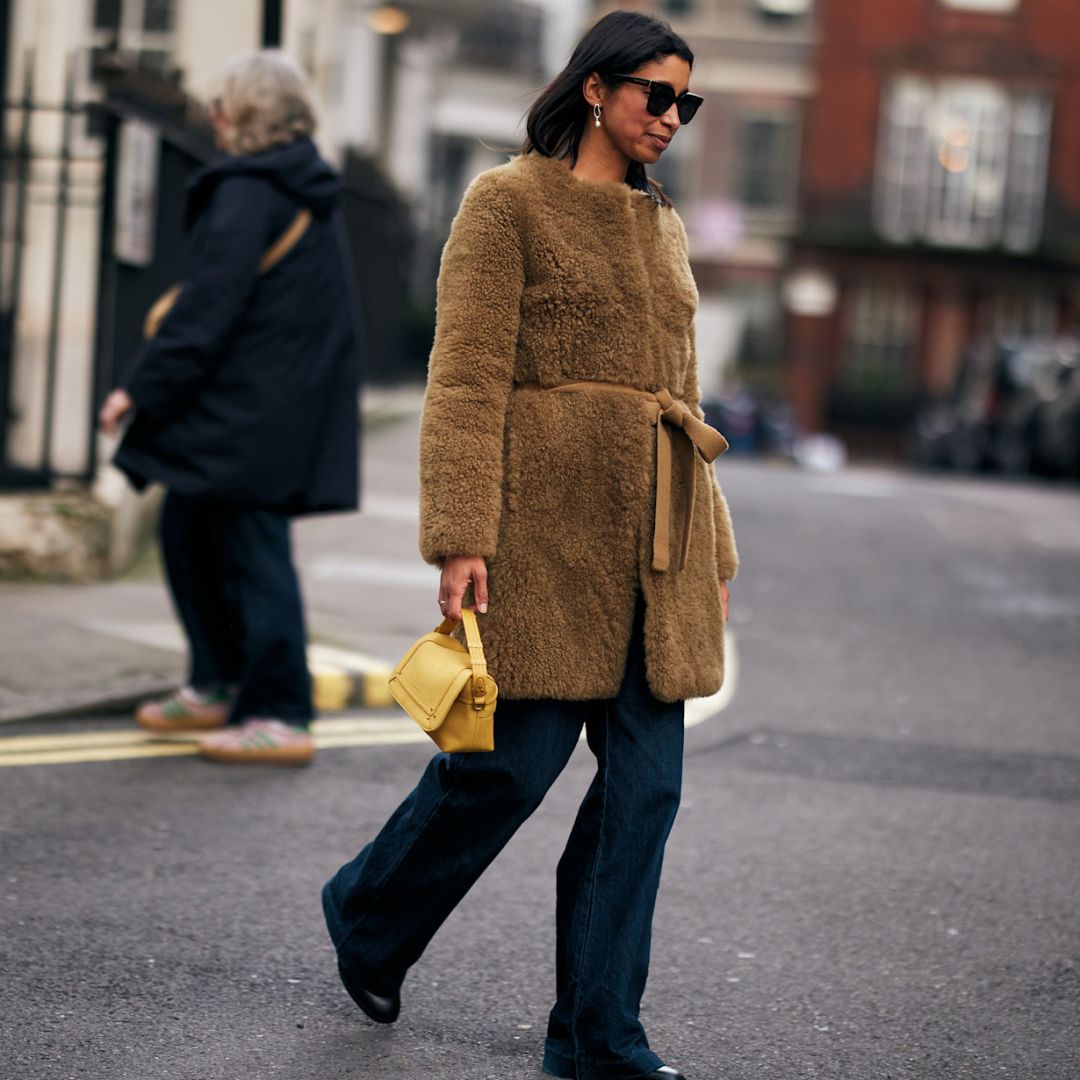 fashion week attendee wearing sunglasses, long faux fur coat, jeans, black boots, and yellow bag