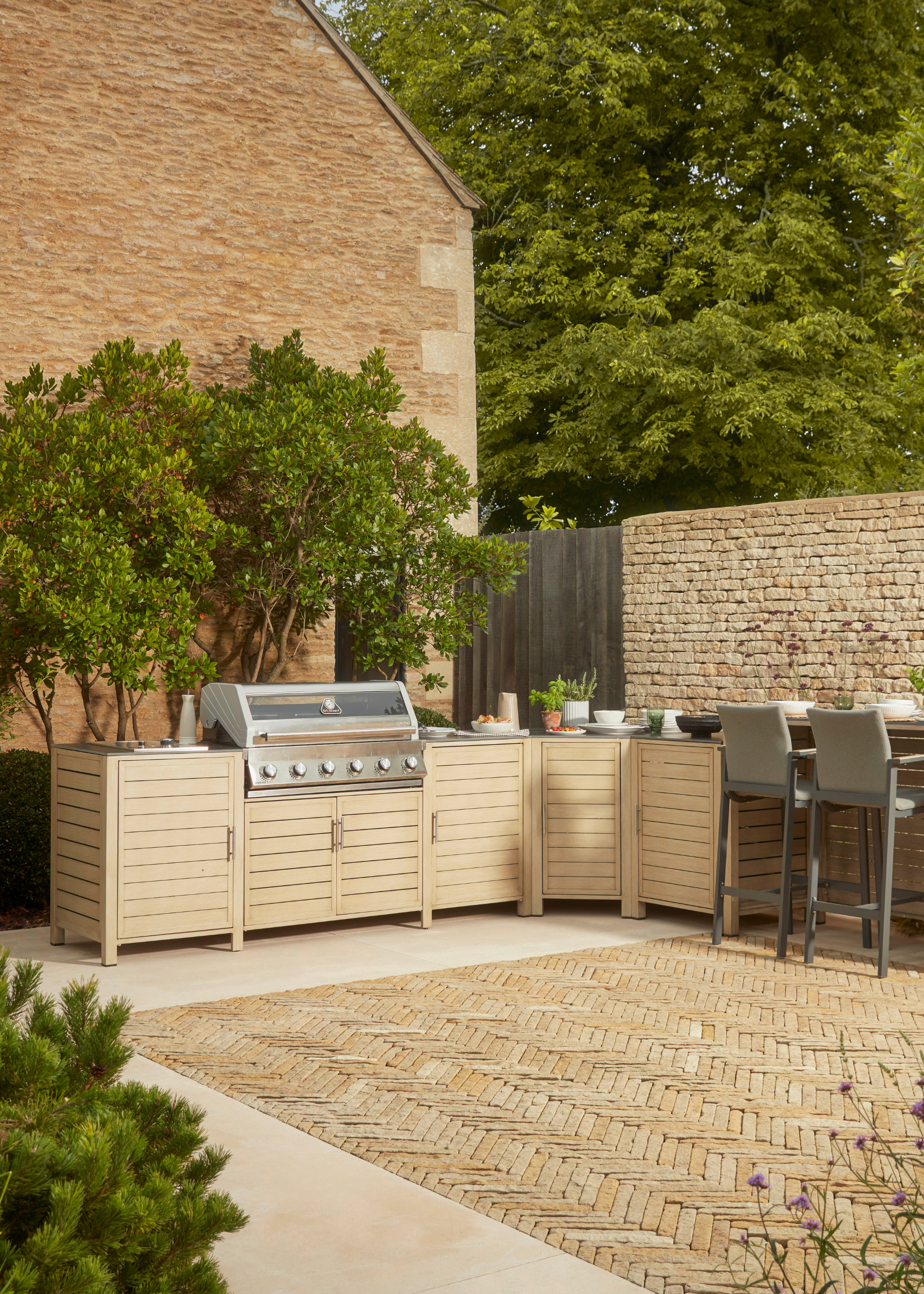 an integrated outdoor kitchen setup with wooden cabinets and an integrated grill, and a bar area