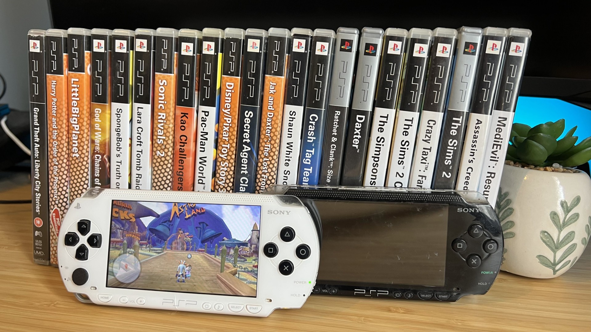 Two PSPs positioned in front of physical game cases on a wooden desk