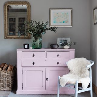 A grey living room with a pink chest of drawers, a wishbone chair and a mirror hung on the wall