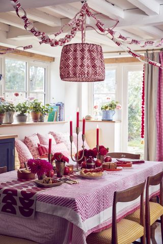 colorful dining room with layered tablecloths in pink and deep red. vases and red candles on the table, pink patterned curtains, paper chains on ceiling