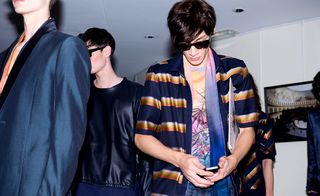 A model glancing at his phone surrounded by other people