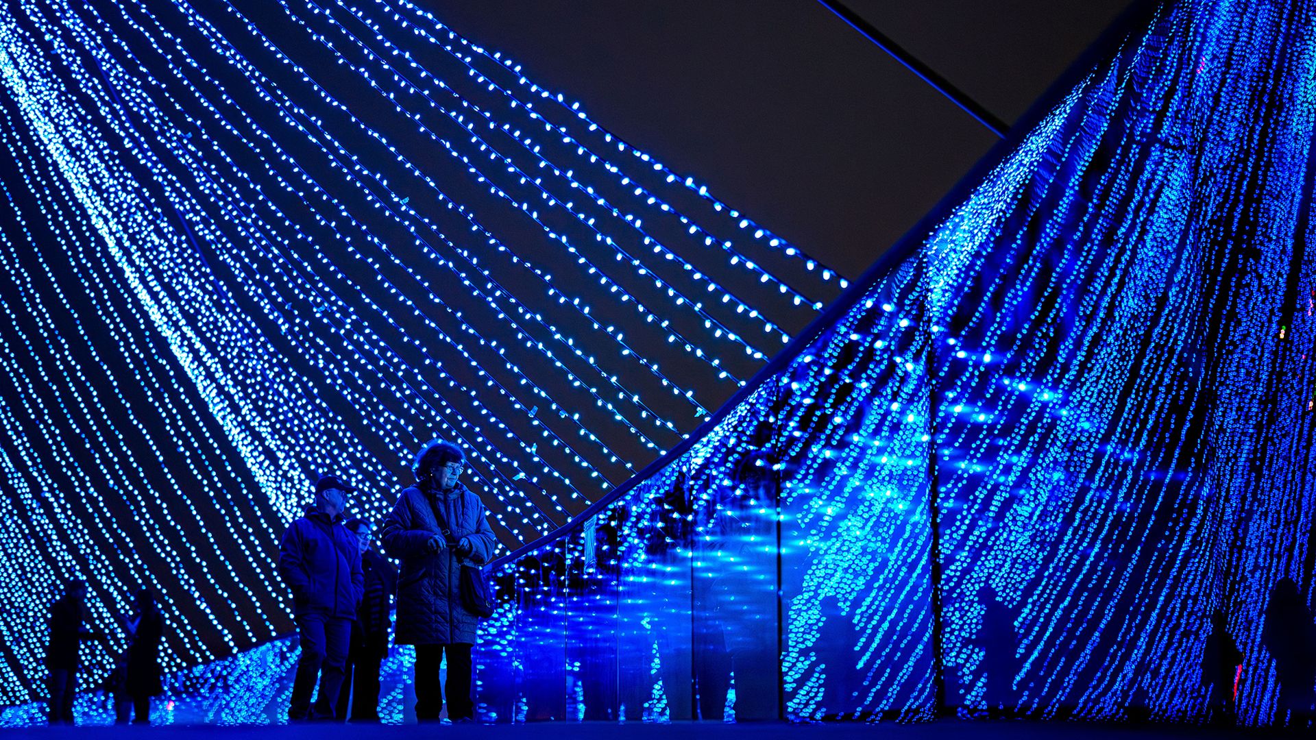 
                                People walk over a bridge decorated with colored lights at a Christmas fair in Bucharest, Romania
                            