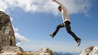 A hiker jumps from one rock to another over a precipice.