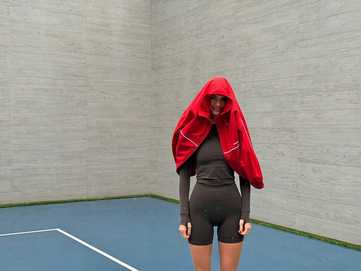 Kendall Jenner in the gym wearing a brown short leggings set from Adanola with white Asics sneakers and a red jacket.