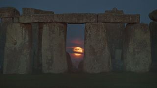 the full moon can be seen between large slabs of stone standing upright