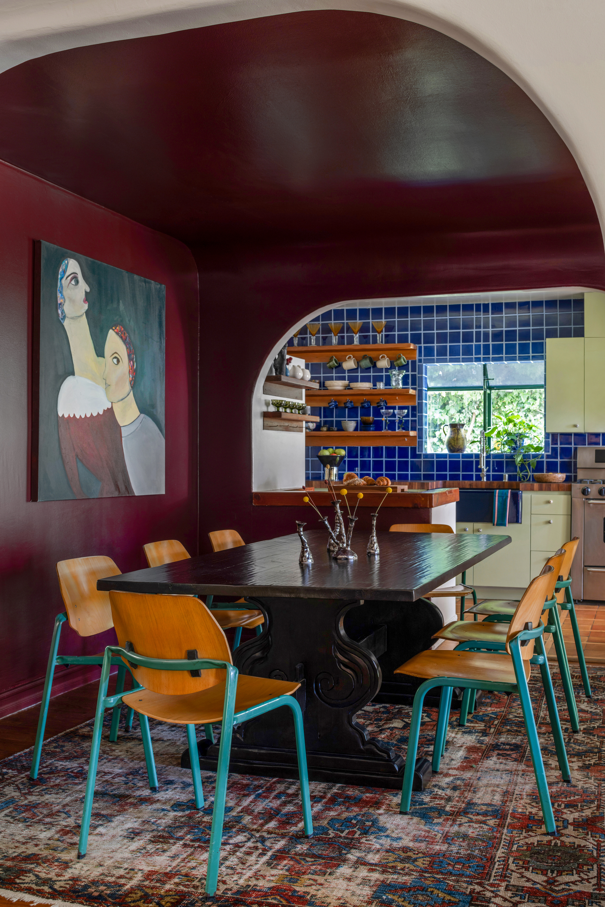 A view of the deep red dining area into the kitchen, an artwork hangs on the wall behind the dining table.