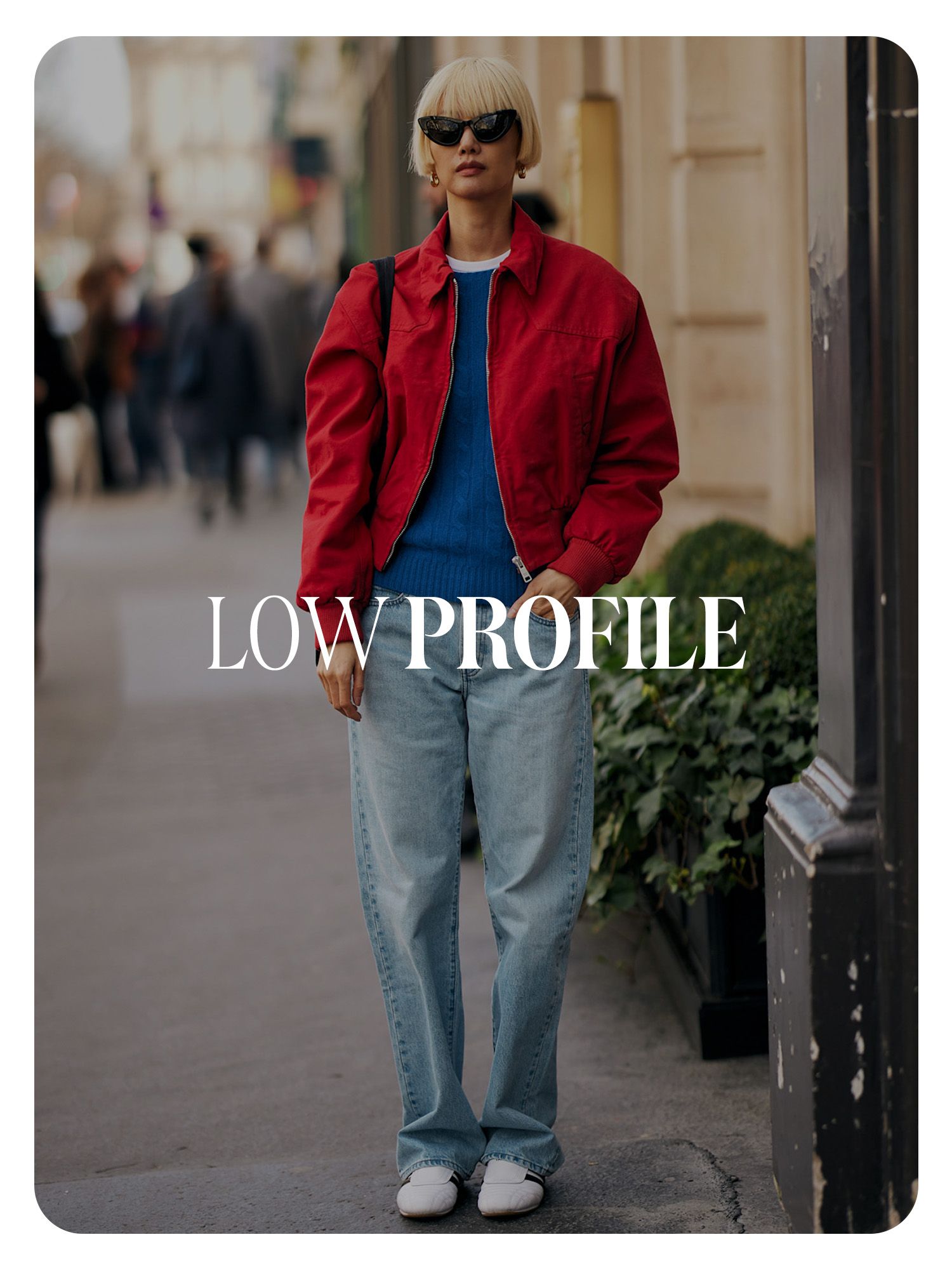 A street style photo of a showgoer wearing a red jacket, jeans, and white, low-profile Adidas sneakers. Text reads, "Low Profile."